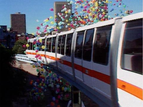 The Sydney monorail on the first day it opened. It glides along on the track with hundreds of multicoloured balloons floating beside it.