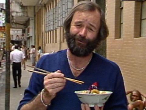 Peter Russell-Clarke eating from a bowl with chopsticks on a busy street.