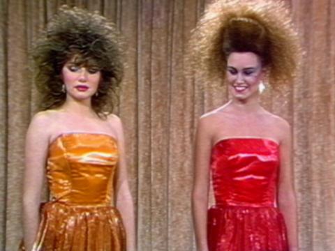 Two models wearing shiny formal dresses and sporting big 1980s hair and make-up.