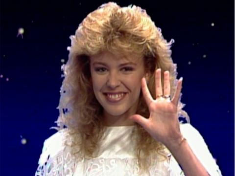 Kylie Minogue with a perm waving at the camera.