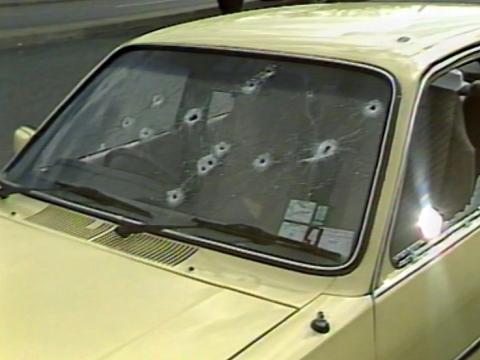 Close up of a yellow car, with a focus on the front windscreen which has multiple bullet holes in it.