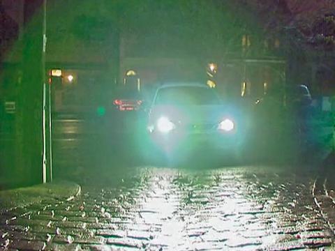 Front of a car with headlights on pulling into a cobblestone street