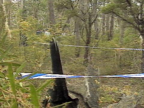 An area of bushland with blue and white police tape woven through it. A group of police officers are standing in the background among some trees and bushes. 