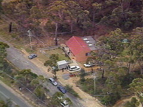 Aerial view of a house surrounded by cars and vans with police tape surrounding it.