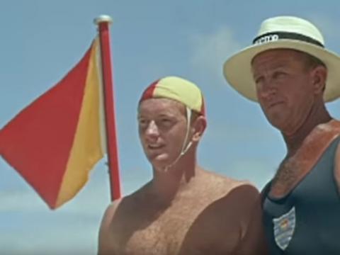 Two lifesavers look out to sea next to a swimming flag