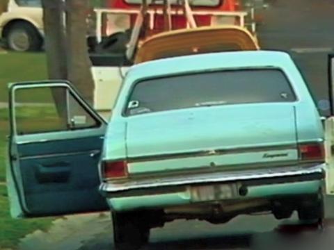 The rear of a pale blue sedan car parked on the side of a road with the passenger side door open. 
