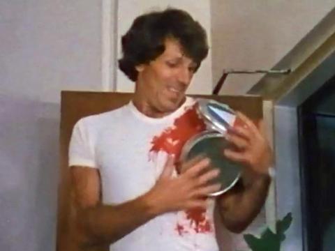 Man in a white T shirt being attacked by a film can and covered in blood.
