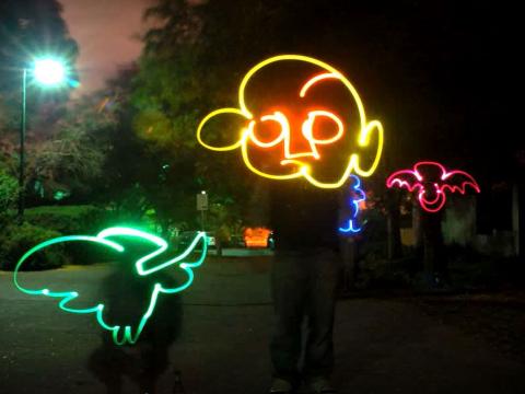 Street scene at night with neon drawings of a face, bird and bat.