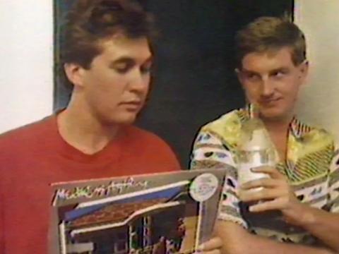Wonder World! reporter Maurice Parker holding a record sleeve. Standing next to him is musician/singer Greedy Smith from the band Mental As Anything. Both pictured from the chest up. 