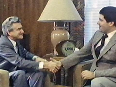 Former Prime Minister Bob Hawke and TV presenter Simon Townsend. Both are seated and looking at one another as they shake hands.