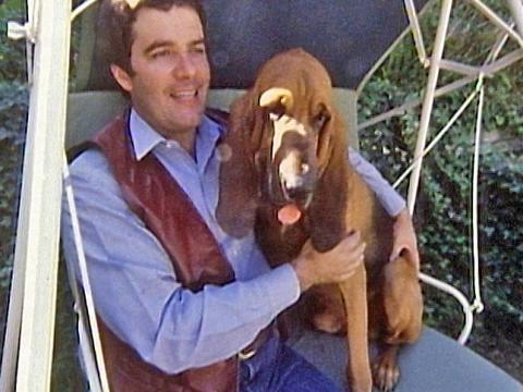 Simon Townsend and his dog Woodrow the bloodhound seated on an outdoor swing.