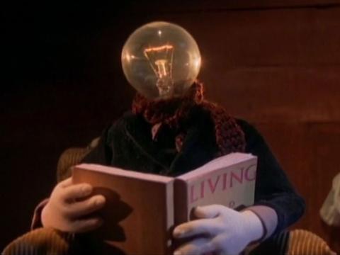 Animation still of a man with a lightbulb head reading a book.