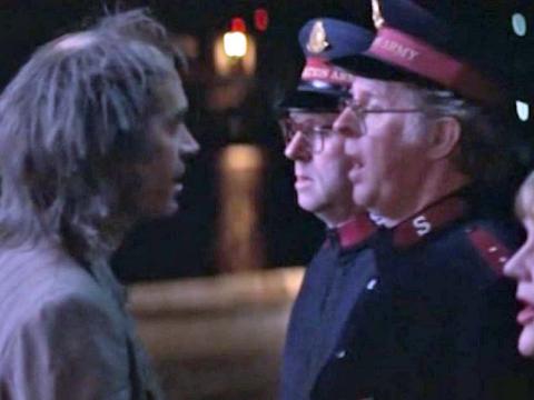 A dishevelled man stands in from of a choir of Salvation Army members at night