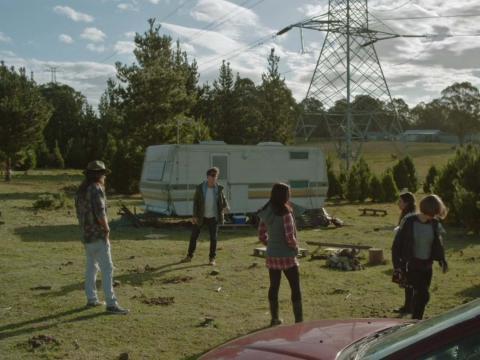 A group of young people standing in a paddock outside of a caravan