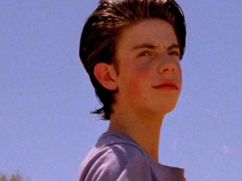 Young boy with black wavy hair and stands against a brilliant blue sky.