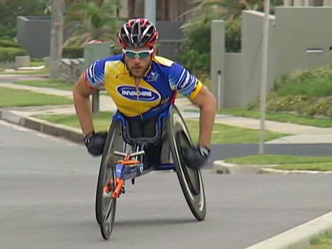 Paraathlete Kurt Fearnley is using a wheelchair to travel down a suburban street.