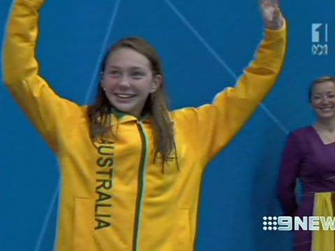 Paralympic swimmer Maddison Elliot holds her arms up in a victory pose. She is wearing an Australian green and gold uniform.