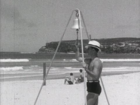 A man stands on a beach ringing a shark warning bell