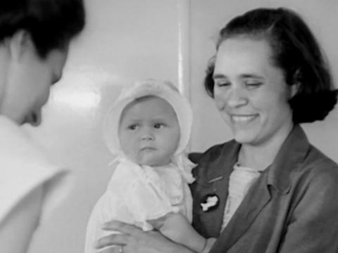 A young woman leaving her baby at a childcare centre. Circa 1940s.