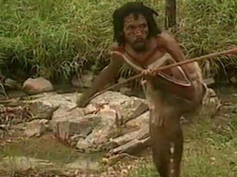 Aboriginal man walking through the bush and holding a spear in his hand