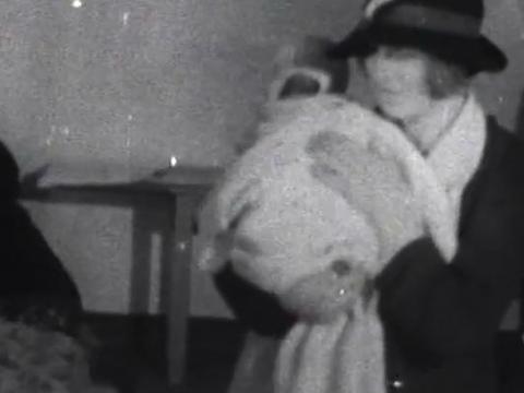 A woman with a baby waits to receive blankets from a volunteer worker, circa 1930s