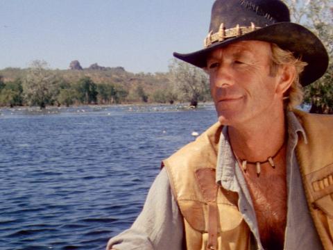 Paul Hogan as Crocodile Dundee steering a boat on a river in the Northern Territory