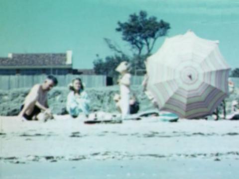 Still from a home movie showing a family playing on the beach
