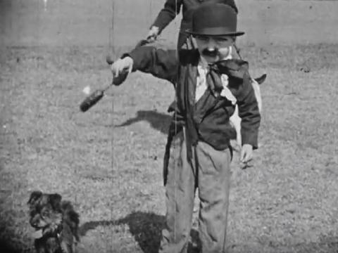 A small boy dressed as Charlie Chaplin holds a sausage