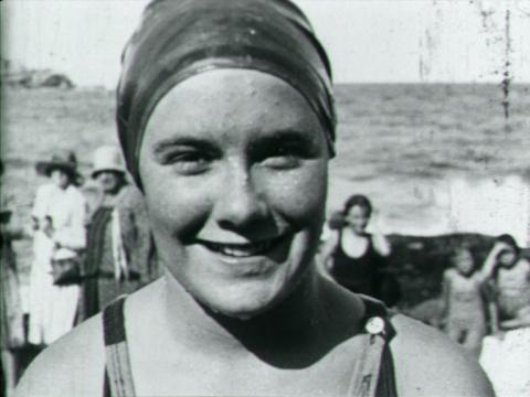 A young woman in a swimming costume smiles at the beach