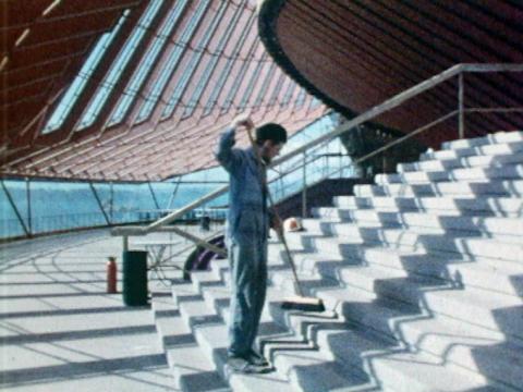 A man is sweeping the steps inside the Sydney Opera House with light streaming through the windows.