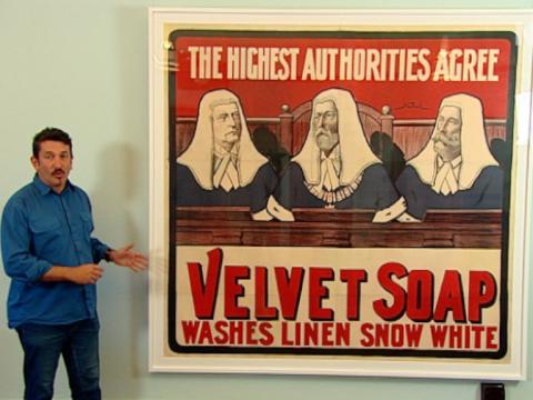 Warren Brown stands next to an enlarged framed print of a Velvet Soap advertisement from 1901.