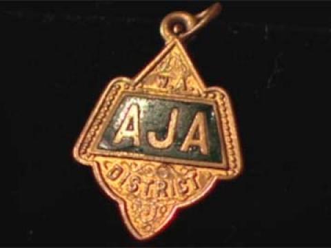 A close-up of John Curtin's Australian Journalists' Association badge against a black background.