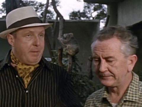 Frank Thring as Doctor Stark in hat and cravat stands next to one his minions.