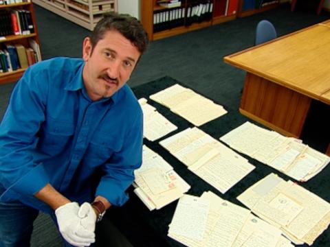 Warren Brown at the National Library of Australia next to a table on which are spread Prime Minster Joseph Lyons' love letters.