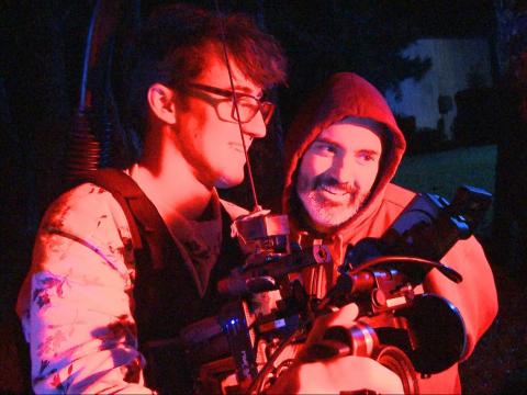 Behind the scenes of two men looking at the video playback on a camera monitor.