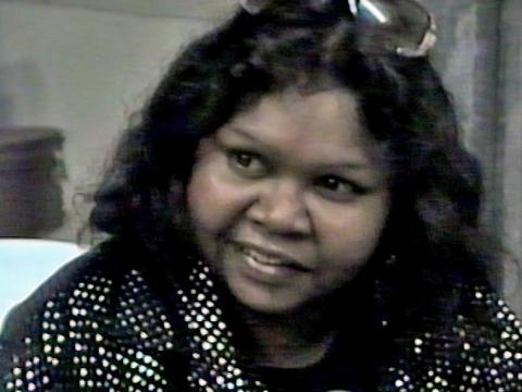Head and shoulders close up of Indigenous songwriter and musician Ruby Hunter, leaning in towards a microphone during an interview.