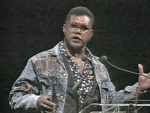 Indigenous musician Archie Roach pictured on a stage at an awards ceremony in front of a microphone, he's holding an award and making a speech.