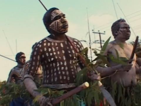 Aboriginal men painted and carrying ceremonial objects performing
