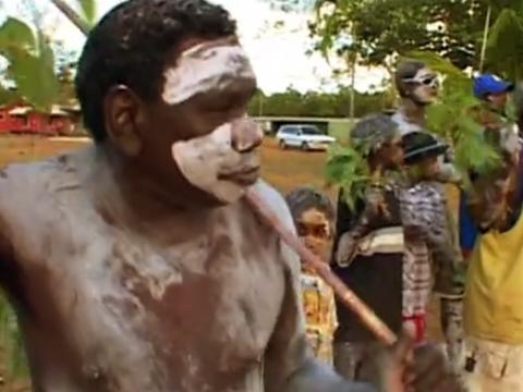 Painted Aboriginal man and others performing a ceremony