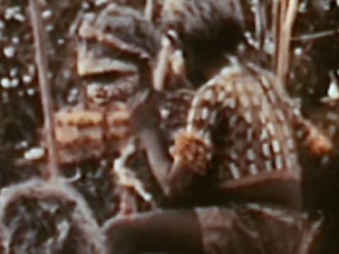 Two decorated indigenous boys on the shoulders of men in a ceremony