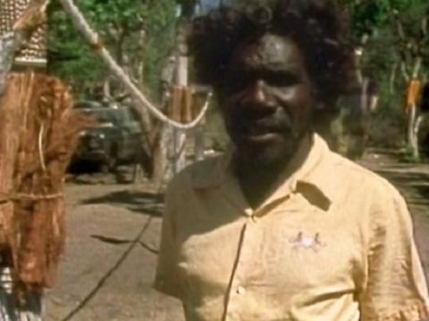 Aboriginal man standing next to ceremonial poles