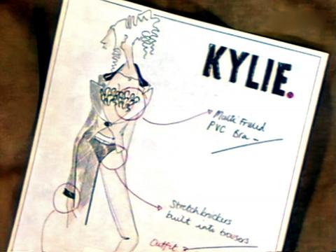 A black and white sketch of a costume design showing a frilled bra, matching pants and sheer top. In the top right corner of the page in bold letters is the name KYLIE.