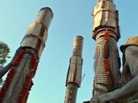 Three totem poles decorated with painting and feathers.