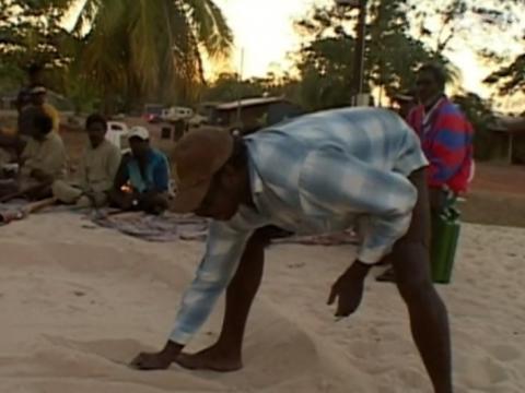 Aboriginal man shaping sand with a stick