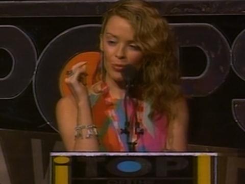 Kylie Minogue is speaking into a microphone at an awards night.