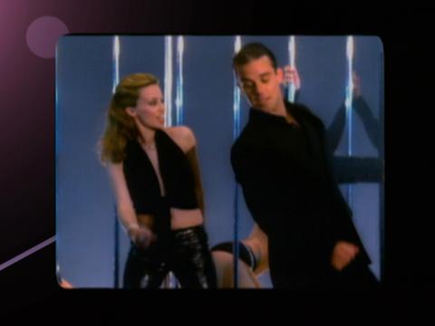 Kylie Minogue and Robbie Williams dance next to each other.