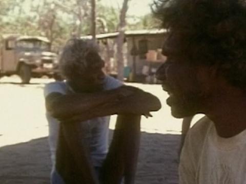 Profile of an Aboriginal man with another seated on the ground in the shade