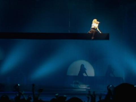 Kylie Minogue appears as a tiny figure on stage performing a live show.