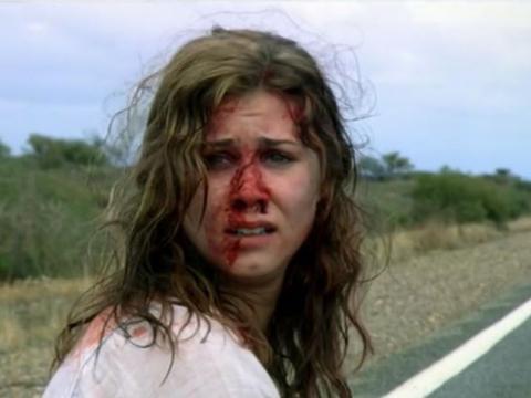 Scared looking young woman with blood on her face on a roadside