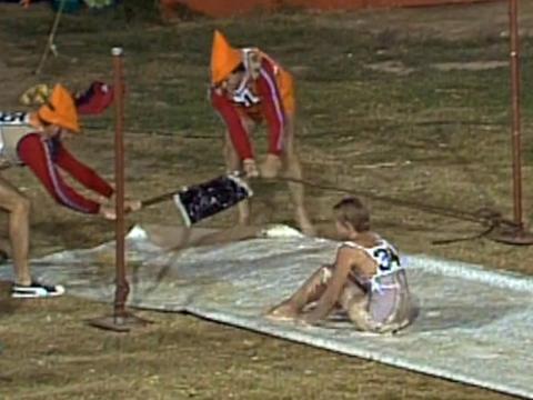 Two men and a woman in a game show doing a physical challenge with a giant catapult and slippery slide